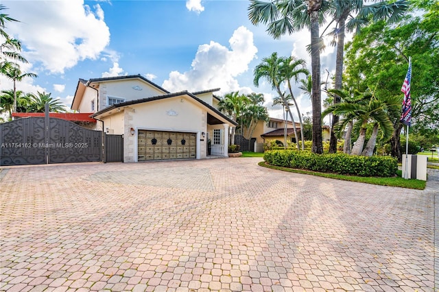 view of front facade with an attached garage, a gate, decorative driveway, and stucco siding