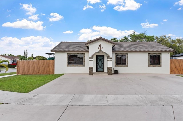 mediterranean / spanish-style house featuring a tiled roof, a front lawn, fence, and stucco siding