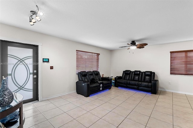 living room with a textured ceiling, ceiling fan, light tile patterned flooring, and baseboards