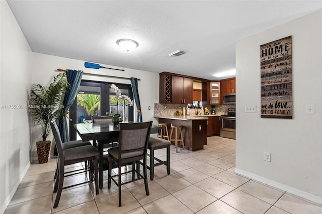 dining room with visible vents, a textured ceiling, baseboards, and light tile patterned floors