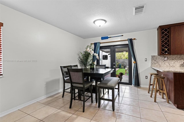 dining room with light tile patterned floors, a textured ceiling, bar area, visible vents, and baseboards