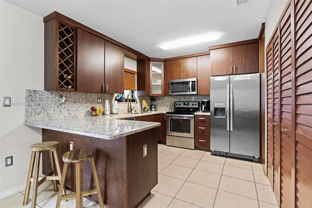 kitchen with light tile patterned floors, decorative backsplash, appliances with stainless steel finishes, a sink, and a peninsula