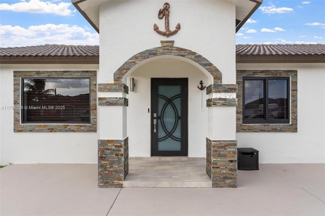 property entrance with stone siding, a tile roof, and stucco siding