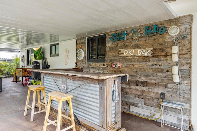 bar featuring concrete floors, wooden walls, and a bar