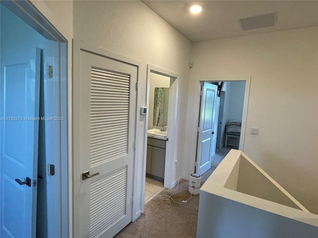 hallway featuring visible vents, a sink, and light carpet