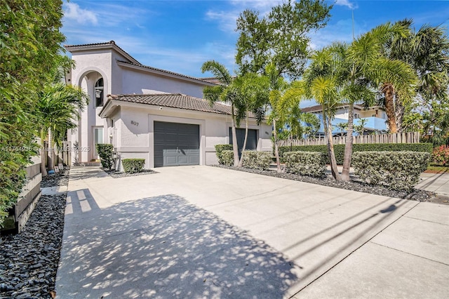 mediterranean / spanish home featuring a garage, concrete driveway, fence, and stucco siding