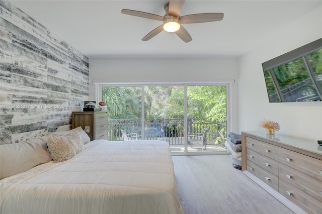 bedroom featuring ceiling fan, access to outside, wood finished floors, and an accent wall