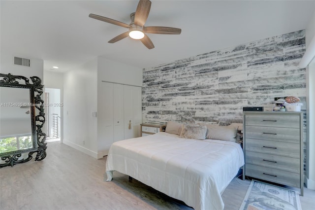 bedroom with wallpapered walls, an accent wall, visible vents, and wood finished floors