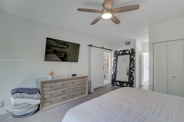 bedroom with a closet, visible vents, a barn door, a ceiling fan, and ensuite bath