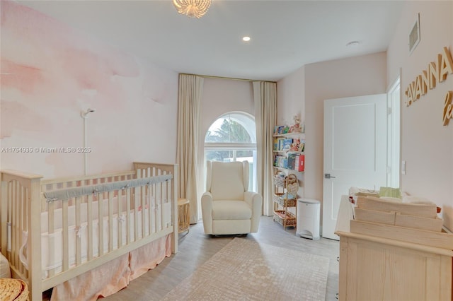 bedroom featuring a nursery area, visible vents, recessed lighting, and wood finished floors