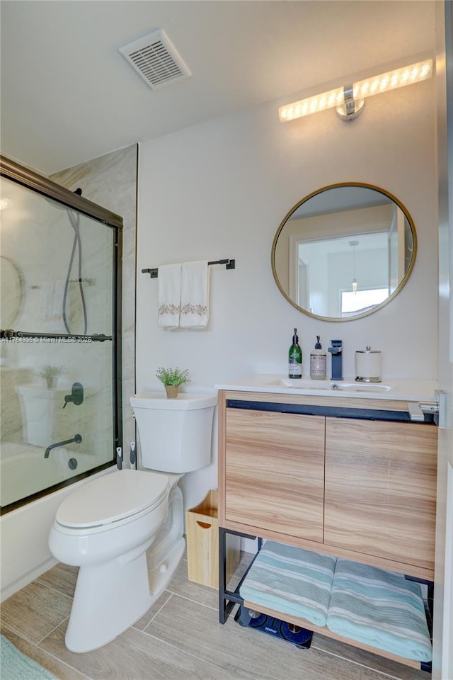 full bathroom featuring toilet, shower / bath combination with glass door, visible vents, and vanity