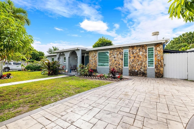 view of front facade featuring stone siding, fence, stucco siding, and a front yard