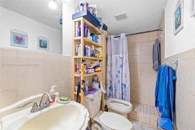 bathroom with visible vents, tile walls, tiled shower, toilet, and a sink