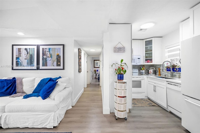 kitchen with white appliances, a sink, white cabinetry, light wood-type flooring, and backsplash