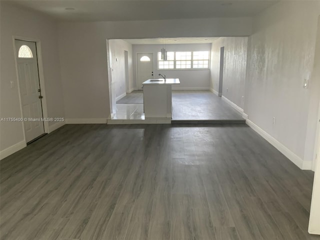 unfurnished living room with wood finished floors, baseboards, and a sink