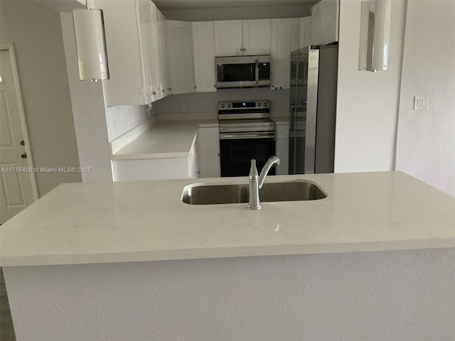 kitchen with stainless steel appliances, a peninsula, a sink, and white cabinetry