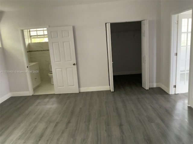 unfurnished bedroom featuring wood finished floors, a closet, baseboards, and connected bathroom
