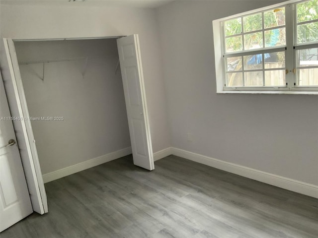 unfurnished bedroom featuring baseboards, wood finished floors, and a closet