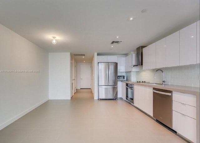 kitchen with stainless steel appliances, light countertops, backsplash, a sink, and wall chimney exhaust hood