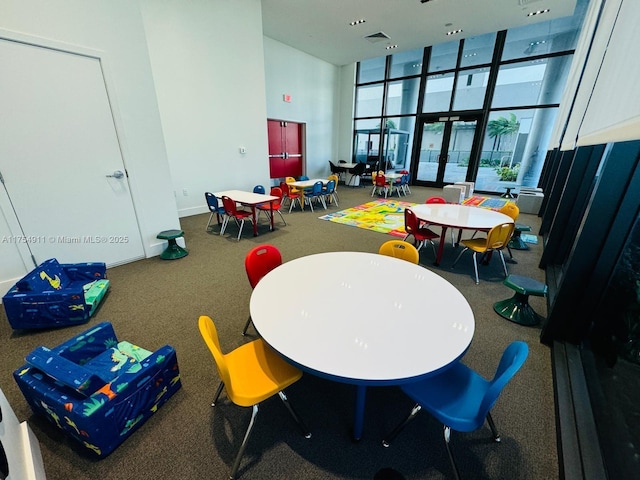 rec room featuring a towering ceiling, visible vents, a wall of windows, and french doors