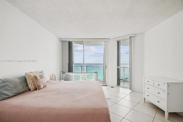 bedroom with a water view, access to exterior, a textured ceiling, floor to ceiling windows, and light tile patterned flooring