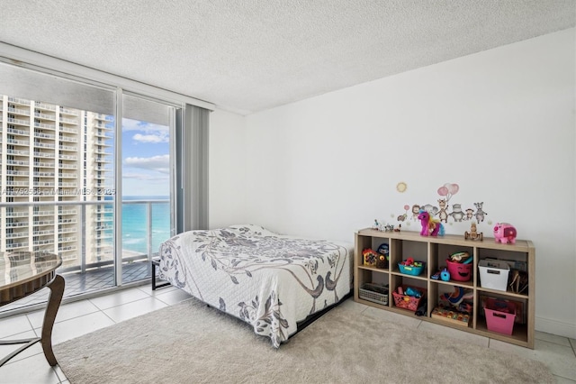 bedroom featuring a textured ceiling, a water view, access to exterior, tile patterned floors, and expansive windows