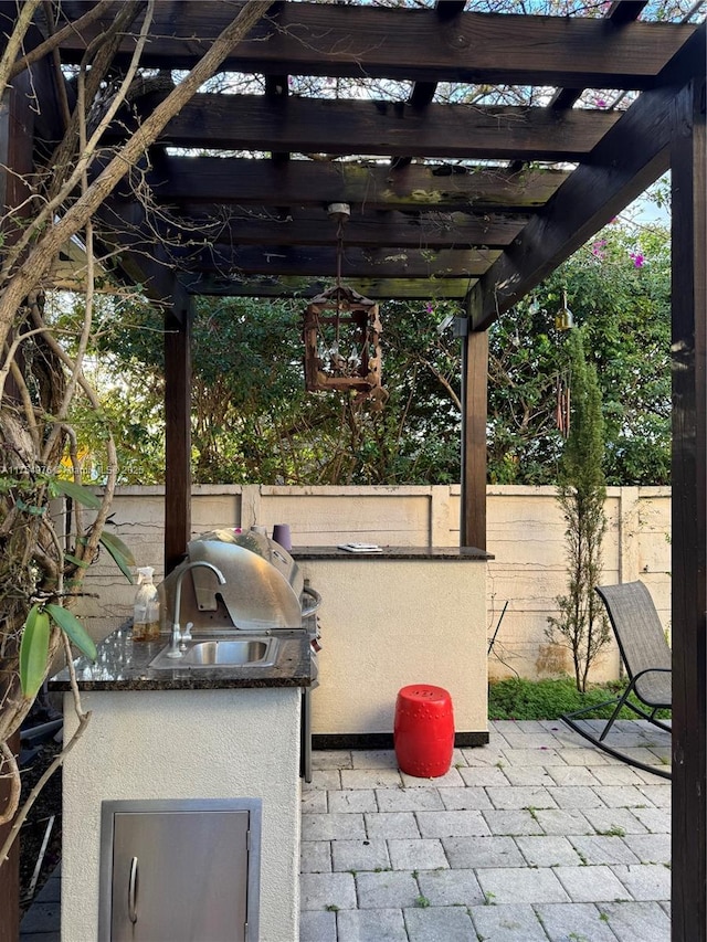 view of patio / terrace featuring area for grilling, an outdoor kitchen, a sink, fence, and a pergola