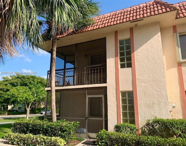 exterior space featuring a tile roof, a balcony, and stucco siding