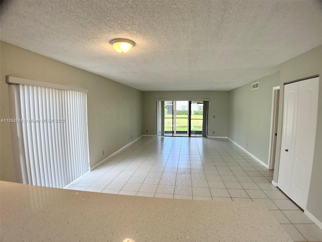 empty room featuring visible vents, a textured ceiling, baseboards, and light tile patterned flooring