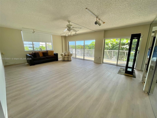 unfurnished living room featuring a ceiling fan, rail lighting, a textured ceiling, and wood finished floors