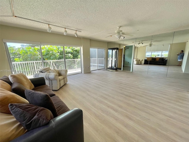 living room featuring a healthy amount of sunlight, light wood-style floors, a ceiling fan, and a textured ceiling