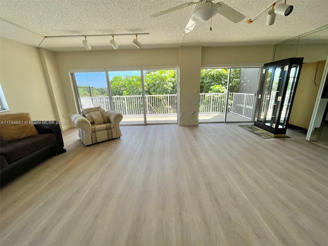 unfurnished living room featuring a ceiling fan, rail lighting, a textured ceiling, and wood finished floors