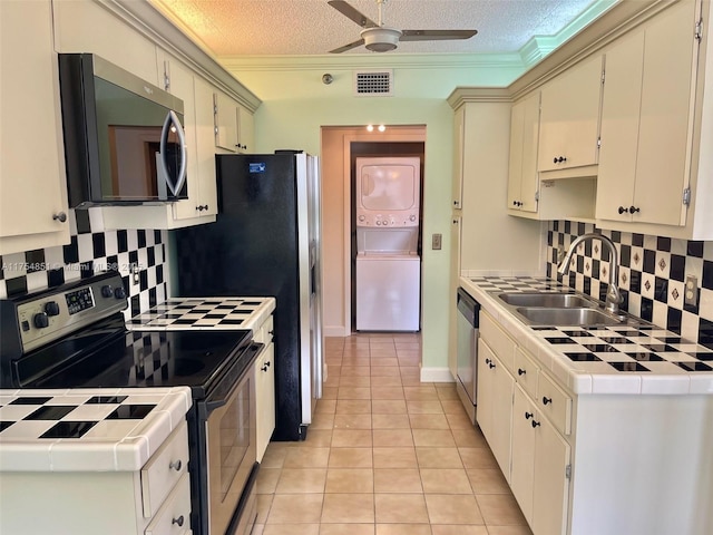 kitchen with appliances with stainless steel finishes, stacked washer and clothes dryer, a sink, and tile countertops