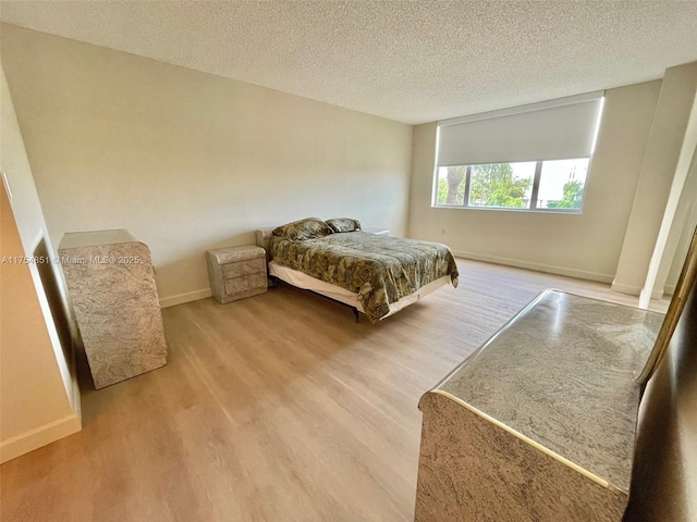 bedroom featuring a textured ceiling, baseboards, and wood finished floors