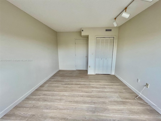 unfurnished bedroom with light wood finished floors, baseboards, visible vents, a textured ceiling, and a closet