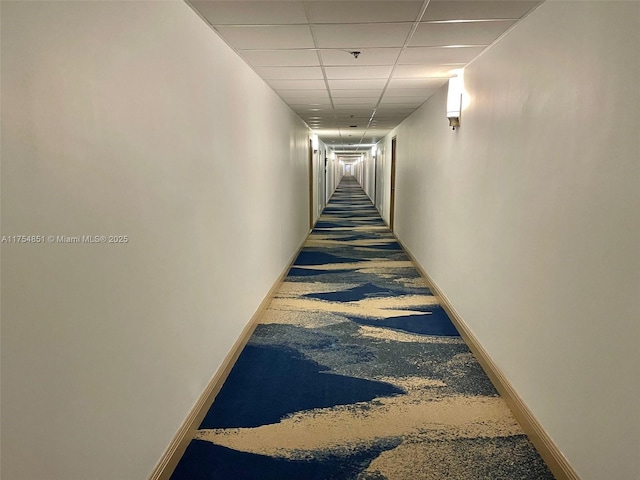 hall featuring a paneled ceiling and baseboards