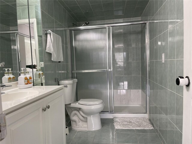 bathroom featuring tile walls, toilet, a stall shower, vanity, and tile patterned floors