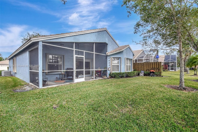 back of property with a sunroom, central AC, a yard, and stucco siding