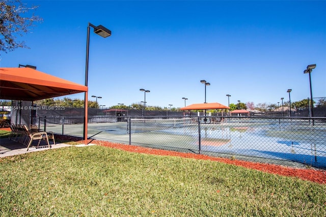 view of tennis court with fence and a yard