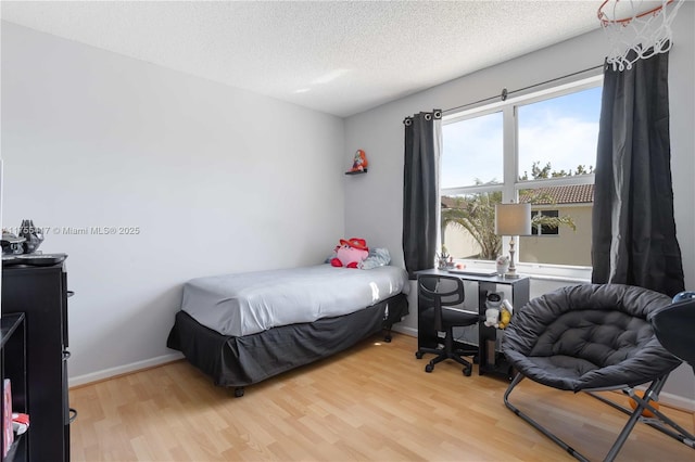 bedroom featuring light wood-style floors, a textured ceiling, and baseboards