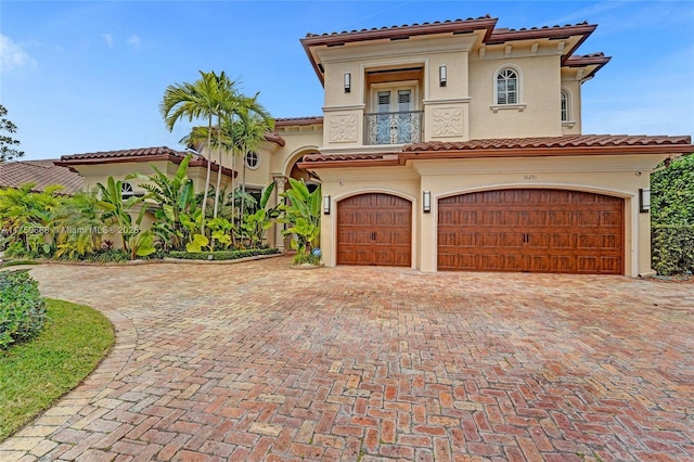 mediterranean / spanish-style house featuring a tiled roof, stucco siding, decorative driveway, a garage, and a balcony