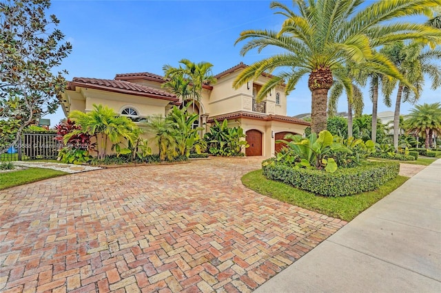 mediterranean / spanish house with stucco siding, a tile roof, decorative driveway, a garage, and a balcony