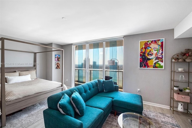 bedroom with access to exterior, baseboards, a wall of windows, and wood finished floors