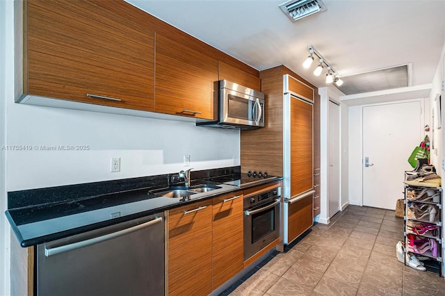 kitchen with appliances with stainless steel finishes, dark countertops, brown cabinetry, and visible vents