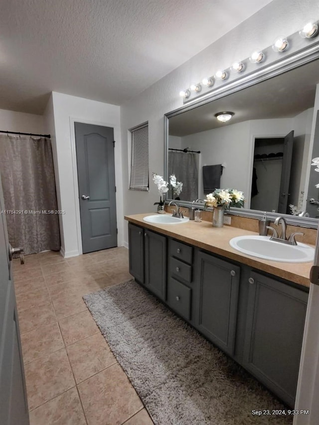 bathroom featuring a sink, tile patterned floors, double vanity, and a textured ceiling