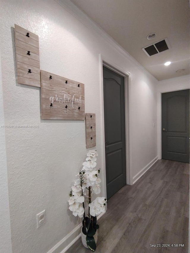 hall featuring visible vents, baseboards, crown molding, and wood finished floors