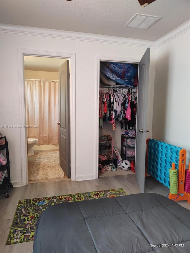 bedroom featuring a closet, ornamental molding, connected bathroom, visible vents, and wood finished floors