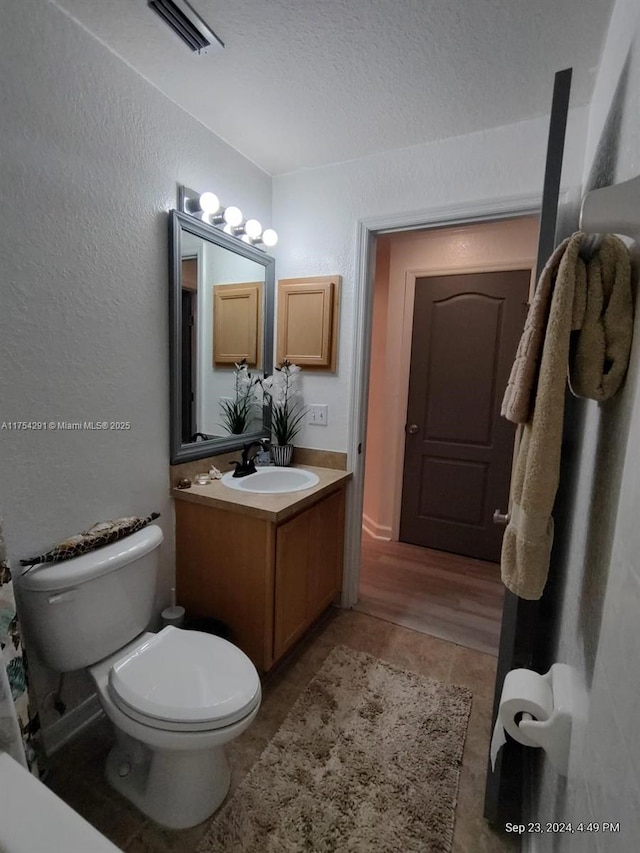 bathroom featuring visible vents, toilet, a textured wall, vanity, and tile patterned flooring