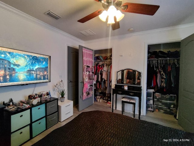 bedroom featuring two closets, visible vents, crown molding, and a ceiling fan