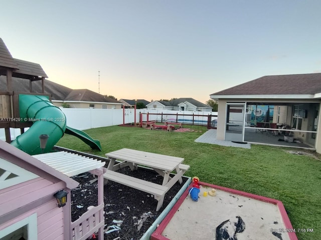 yard at dusk with a fenced backyard, a playground, and a sunroom